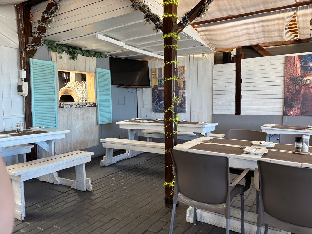 interior view of little sicily restaurant in jeffrey’s bay, tables in the foreground, pizza oven in the background, the decor is light and slightly beachy 