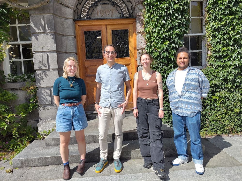 a group hoto four people (woman, man, woman, man) standing infront of a door on a stone building covered with ivy. The words 'School of Botany' are written on the building. 