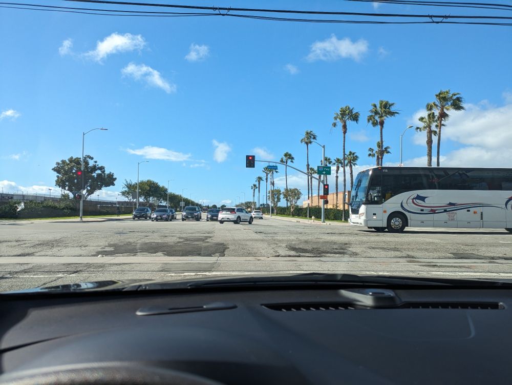 A picture of an intersection. There are palm trees lining the roads. A few clouds dot the blue sky