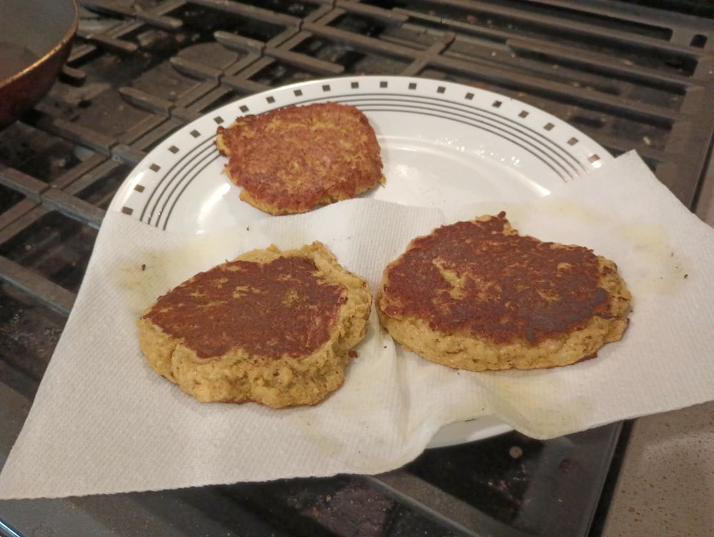 A plate sits on the (extinguished) ranges of a stove. Upon it are three squash fritters, yellow in color from the type of squash and the turmeric. They have a lovely golden brown top surface, though, from their 2 minutes in olive oil (per side). A couple are still sitting on paper towel to blot off some of the oil.