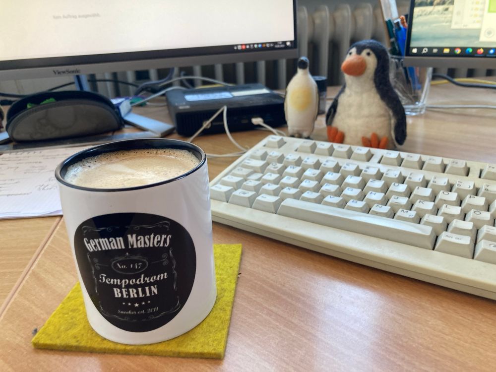 Kaffeetasse „German Masters“ mit Tastatur, Bildschirmen und zwei Pinguinen im Hintergrund 
