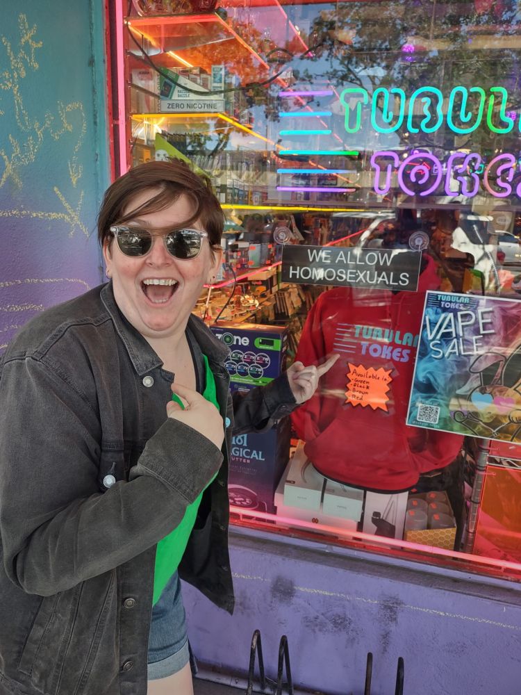 Joyous and fat, Meaks is delighted they are allowed at a vape shop in St. Petersburg, gleefully pointing at a window sign that says "we allow homosexuals" 