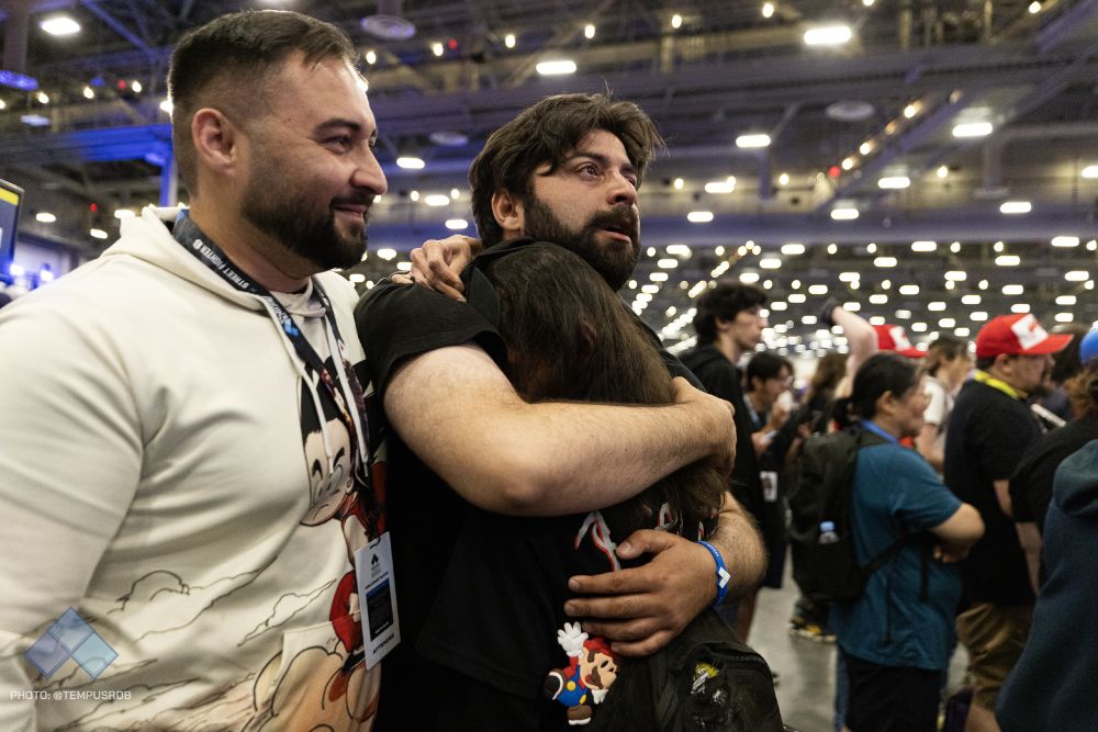 A teary-eyed man hugs a woman after winning his pool. They are standing next to another smiling friend. 
