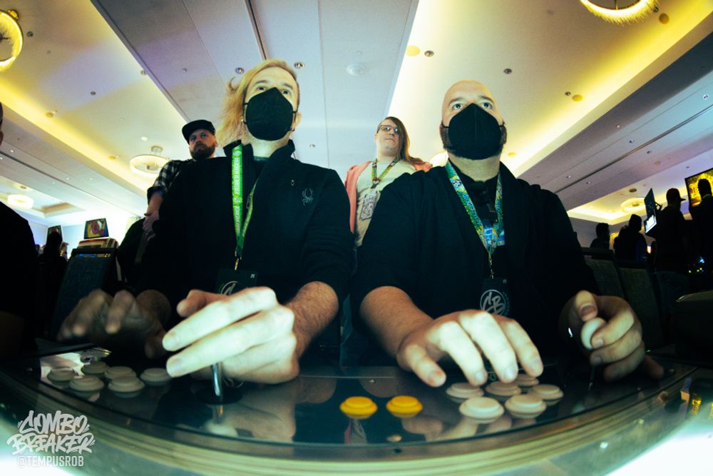 Fisheye photo of two people playing at an arcade cabinet, from the perspective of the screen.
