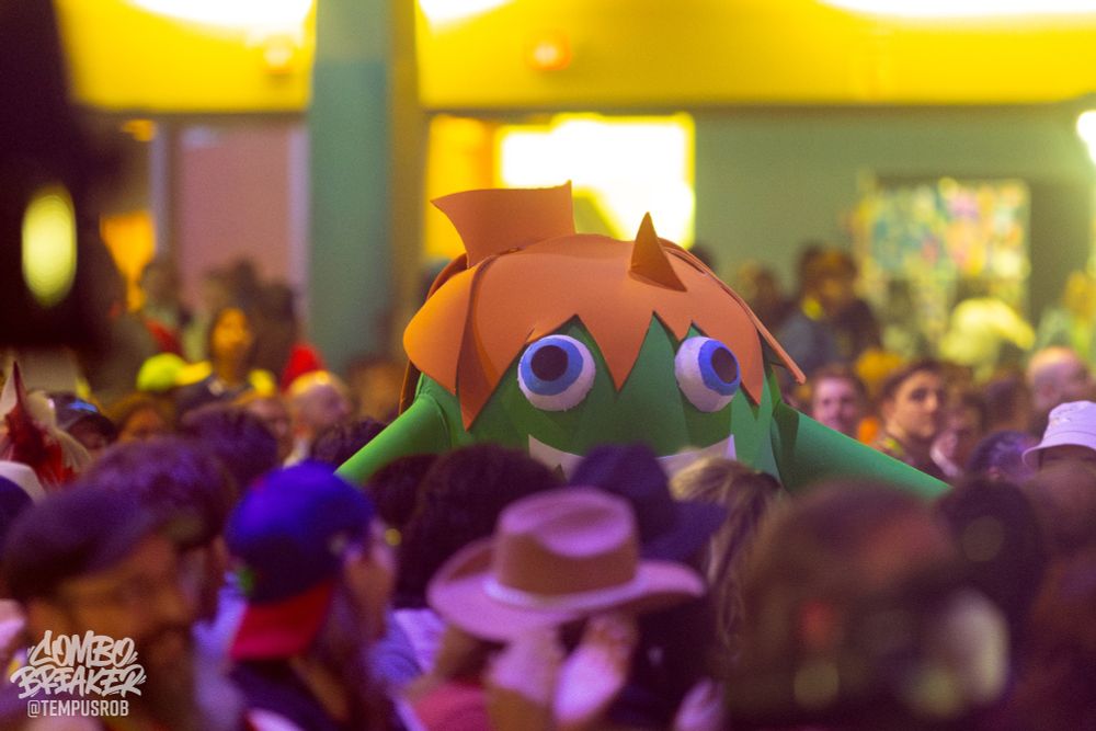Photo of a Blanka-chan cosplayer in the crowd. The costume's head and eyes peek over the heads of the seated audience.