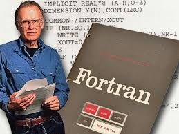 Composed image of John Backus next to a book titled FORTRAN. In the background, there is some FORTRAN code