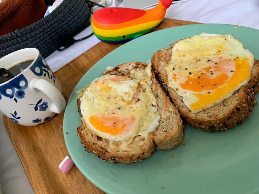 dienblad met twee geroosterde boterhammen met gebakken ei en kaas, een kop koffie, een stressbal in de vorm van een walvis met regenboogkleuren en twee soorten medicatie