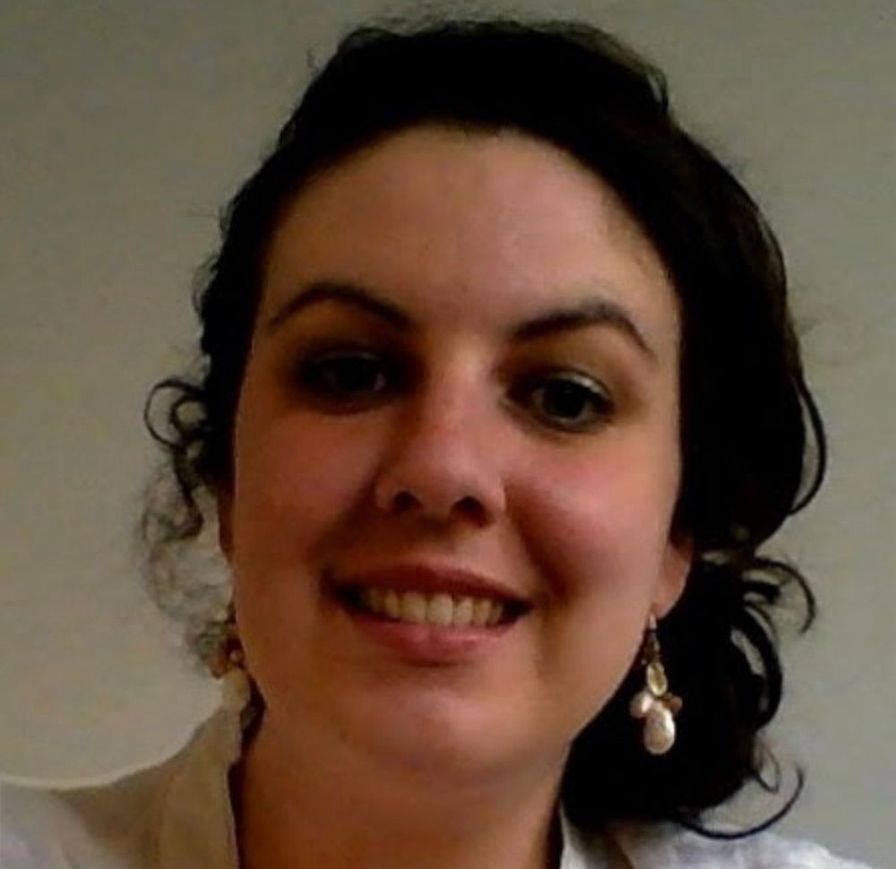 Selfie van mij uit 2014. Ik heb donker krullend haar met een knot aan de zijkant achter mijn oor. Ik draag een witte blouse en hangers in mijn oren