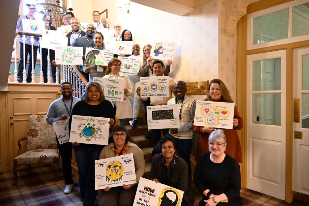 Global Academy Crucible participants with their illustrated research posters, completed by Vanessa, who is sat in the bottom right of the picture