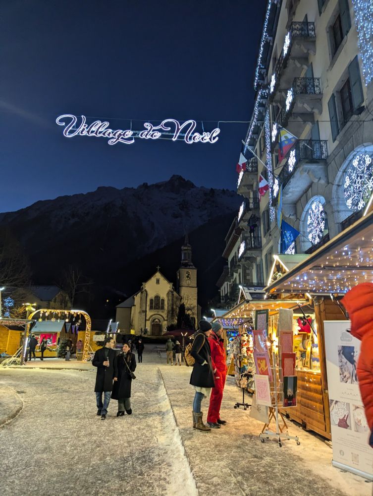 Night view of the Christmas village with lit up booths. Also can see a pretty church with mountains in the background