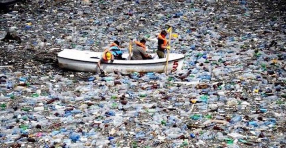 A boat being paddled through a huge mass of floating water bottle plastic
