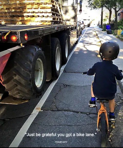 “just be grateful you got a bike-lane.” (Kid on bike in painted bike-lane next to massive truck creeping over the painted line)