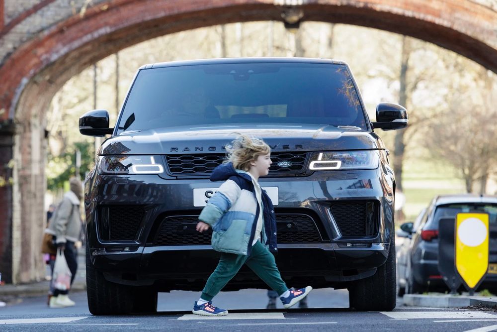 Picture of vehicle hood taller than a little girl crossing in front of it.