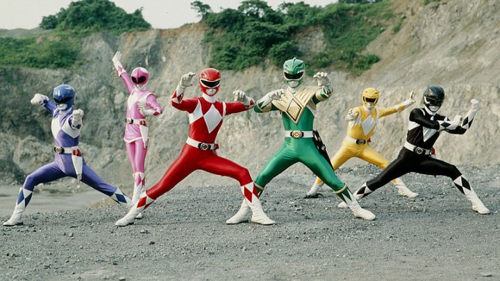 This screenshot depicts the Mighty Morphin Power Rangers posing together in a team line-up. From left to right are the blue, pink, red, green, yellow and black rangers. The background is a rock quarry.