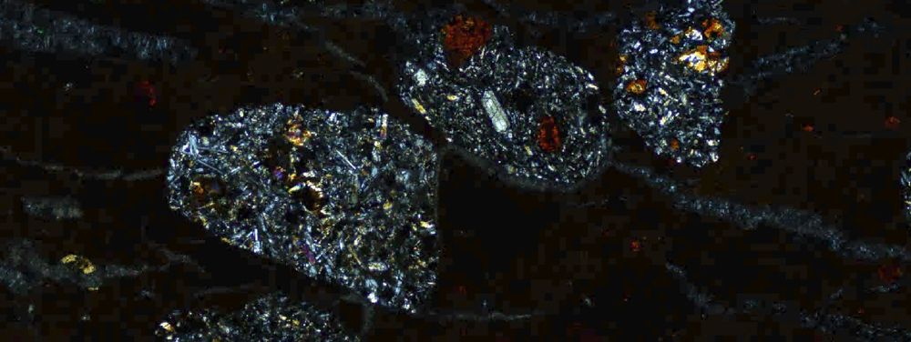 A cross polarised light image under 10x magnification with feldspars, pyroxene and degraded olivine crystals in lithic fragments.