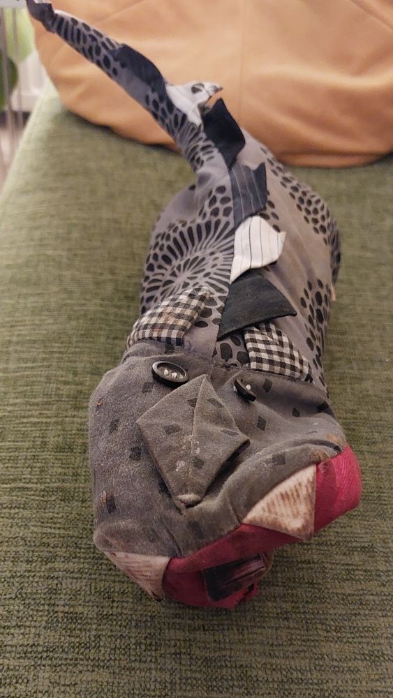 Amatöörin ompelema uunikinnas, julla on lohikäärmeen muoto. Punainen kita, jossa kieli, harmaamustassa
 vartalossa on selässä eviä (?), häntä on pitkä. Kidan päällä on nappisilmät, napeista toinen on haljennut rikki. Monessa kohtaa näkyy nokea tai tummia tahroja