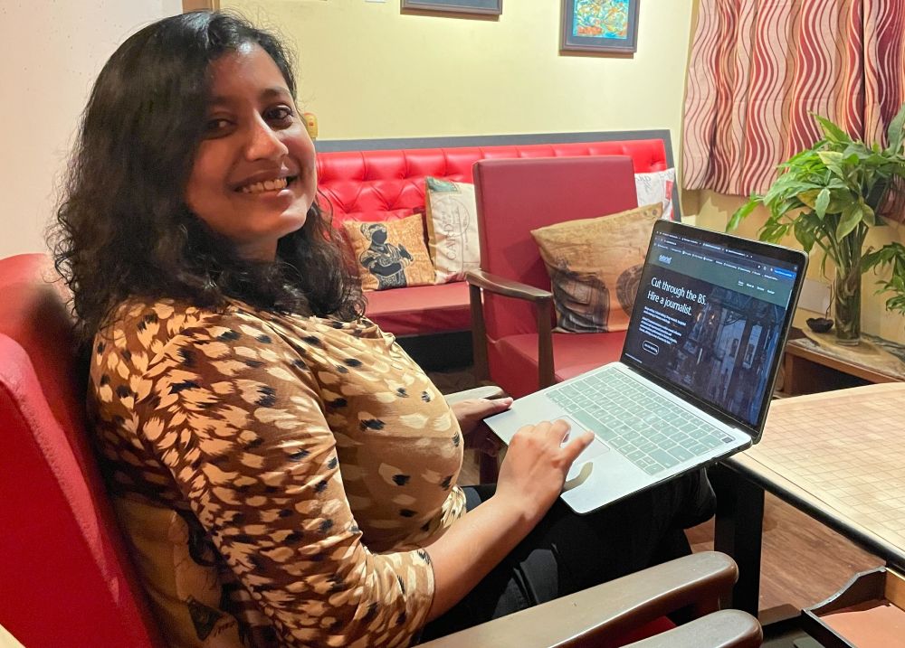 Person sitting in a red chair holding an open laptop that shows the website debriefcomms.ca