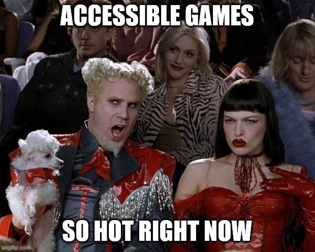 A white man in a curly wig and red suit holding a small poodle in his arm. He's leaning over to his friend, a white woman with red lipstick and black hair and a red outfit saying, "Accessible games, so hot right now."
