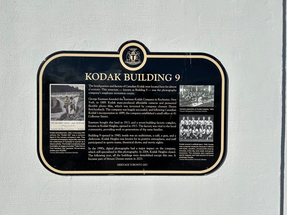 Heritage Toronto plaque:

KODAK BUILDING 9
The headquarters and factory of Canadian Kodak were located here for almost a century. This structure — known as Building 9 — was the photography company's employee recreation centre.
George Eastman founded the Eustman Kodak Company in Rochester, New York, in 1889. Kodak mass-produced affordable cameras and pioneered flexible photo film, which was invented by company chemist Henry Reichenbach. The company was hugcly successful, and following Canadian Kodak's incorporation in 1899, the company established a small office at 41
Colborne Street.
Eastman bought this land in 1913, and a seven-building factory complex, known as Kodak Heights, opened in 1917. The factory was vital to the local community, providing work to generations of the same familics.
Building 9 opened in 1940; inside was an auditorium, a café, a gym, and a darkroom. Kodak Heights was known for its positive atmosphere, and staff participated in sports teams, theatrical shows, and movie nights.
In the 1990s, digital photography had a major impact on the company, which still specialized in film photography. In 2004, Kodak Heights closed.
The following year, all the buildings were demolished except this. 