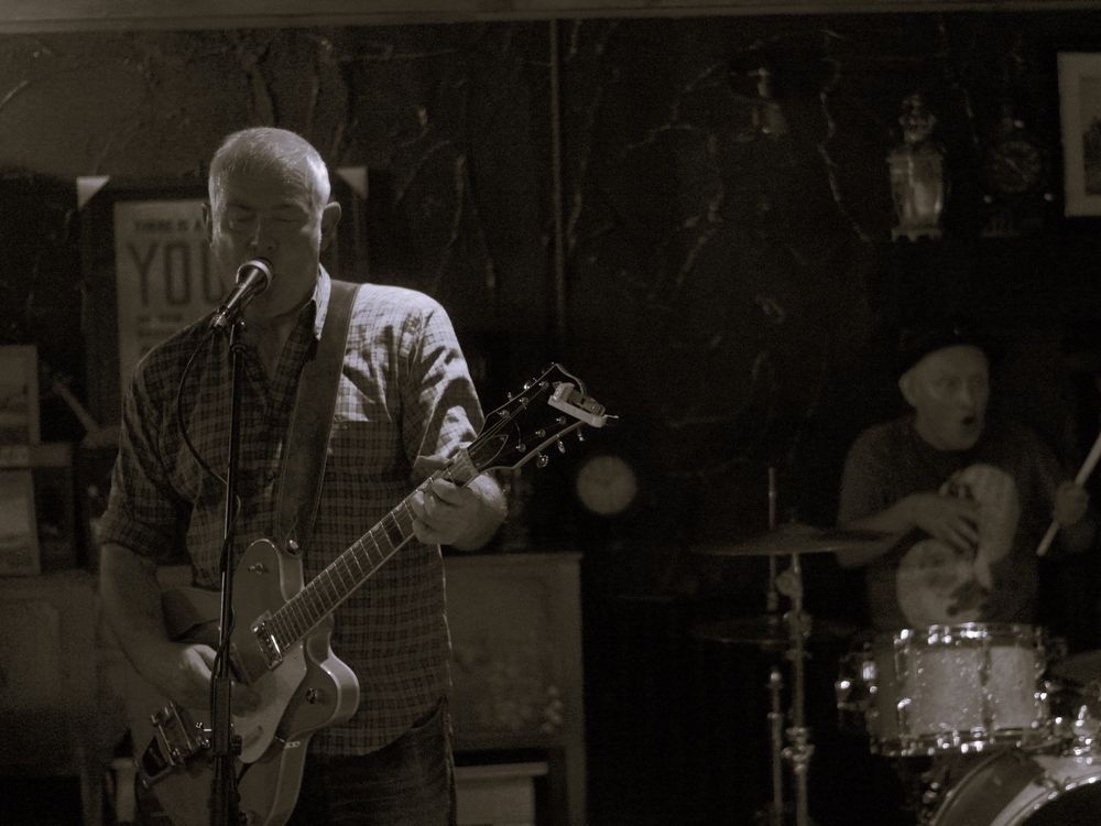 Dave and Daren performing in Kirkcaldy, Dave on guitar and singing, Daren doing some interpretative mime drumming.