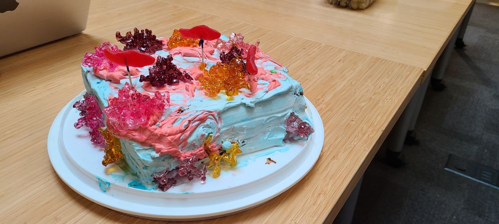 Cake decorated to look like a coral reef. The frosting is blue and the corals are made out of melted sugar. There are Swedish Fish candies swimming through the sugar corals.