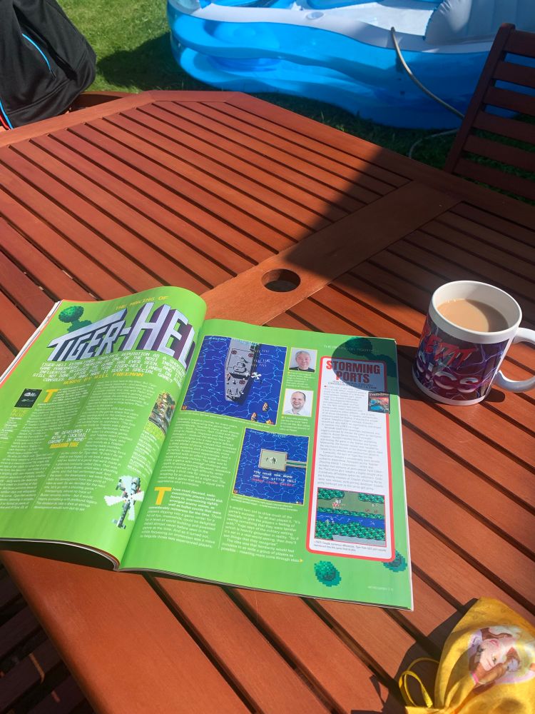 Double page spread about Tiger Heli from retro gamer magazine on a table outside, with a cup of tea next to it.