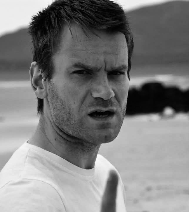 Scowsh scowling and wagging a finger at the photographer with a beach and sea in the background