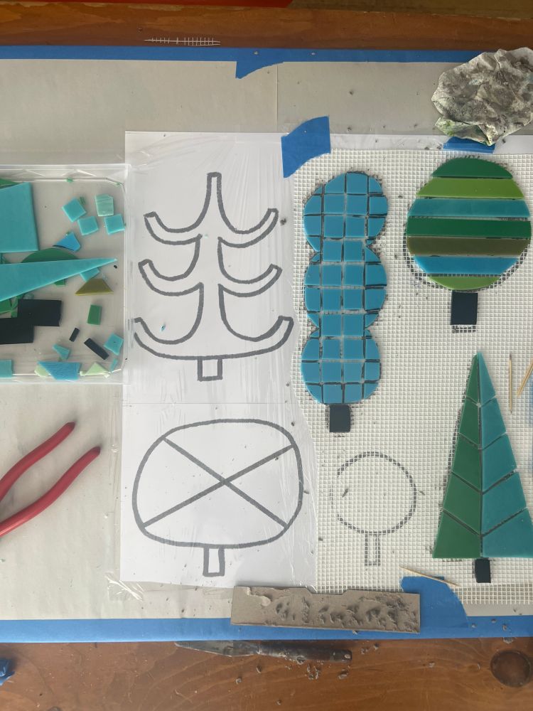 Worktable overhead of mosaic project in progress. Blues and green stained glass creating tree shapes. 