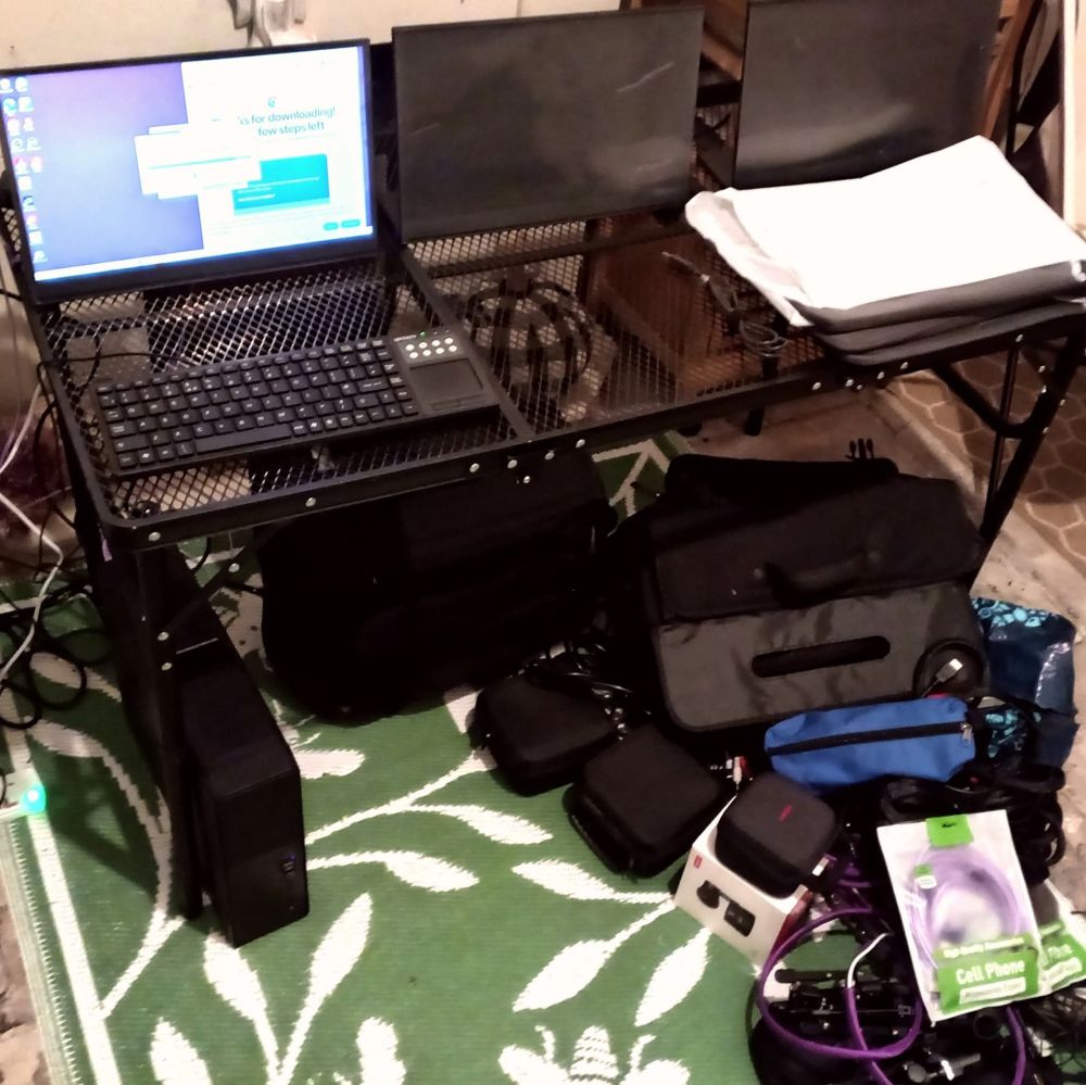 A fold-out table with a PC and three portable monitors, and assorted bags of cables.
