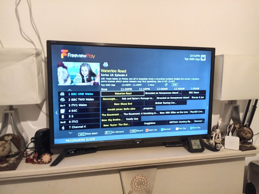 A Freeview TV on a mantlepiece, showing the Freeview Play TV guide, and listings for BBC ONE Wales, BBC TWO Wales, ITV1 Wales, S4C, 5, ITV2, Channel 4.