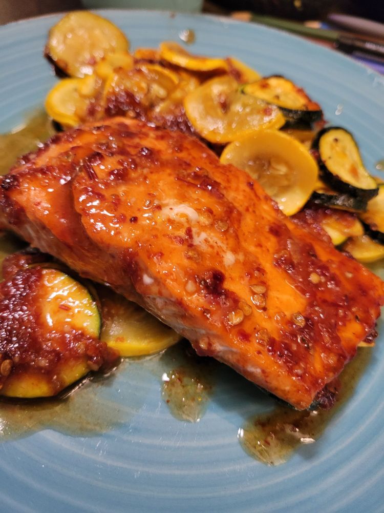A blue plate with roasted, sliced zucchini and yellow squash, topped with a serving of salmon- all covered in a red chipotle honey adobo garlic puree.