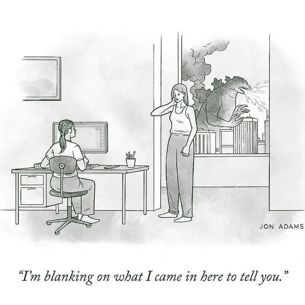 A woman standing next to another woman sitting at a desk, stating "I'm blanking on what I came in here to tell you." while we can see out a window in the background that Godzilla is destroying the cityscape.