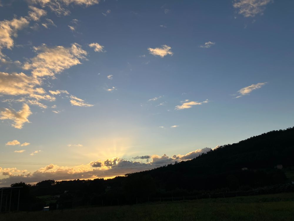 Los rayos de sol se escapan entre una cadena de nubes que ascienden por la ladera del monte. Más arriba, el cielo azul con pequeñas nubes amarillas como algodón deshilachado.