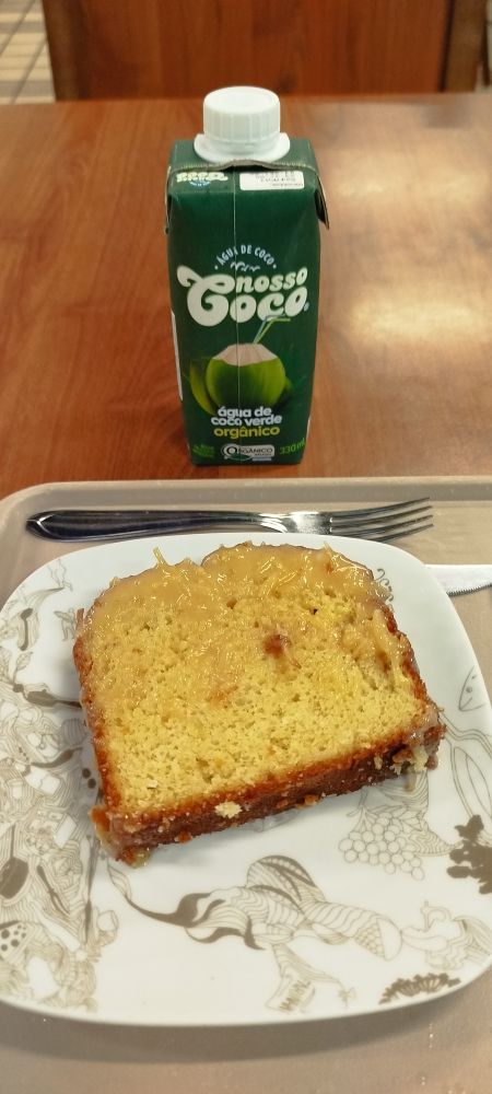 Prato com uma fatia de bolo, e uma caixinha de água de coco à frente.