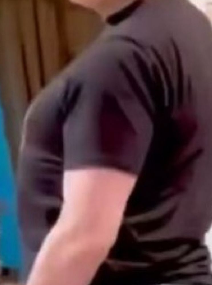 Zoomed in version of the photo, showing soft panels printing through on the front of his torso, a strap printing through his shoulder area, and panels printing through the back of the shirt