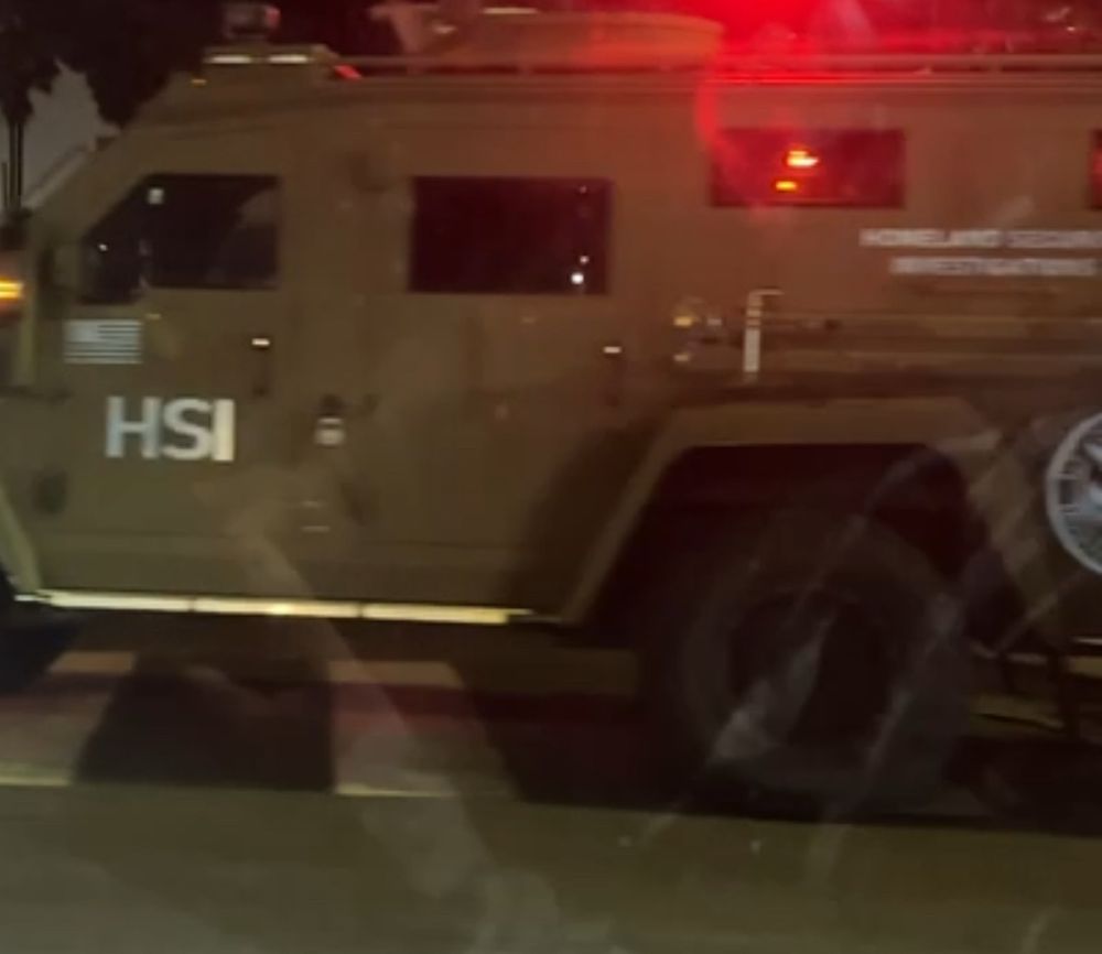 An army green DHS HSI armored vehicle blocks the street