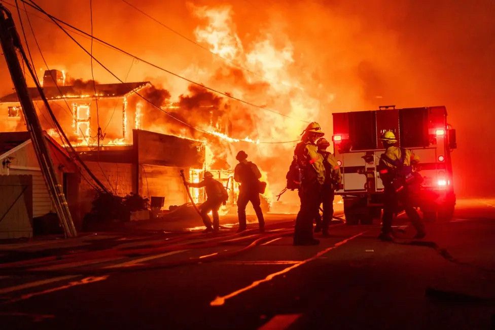 Firefighters stand silhouetted in front of a massive fire engulfing several homes