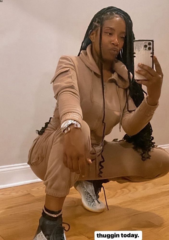 girl crouched down taking selfie in tan sweatsuit with long braids 