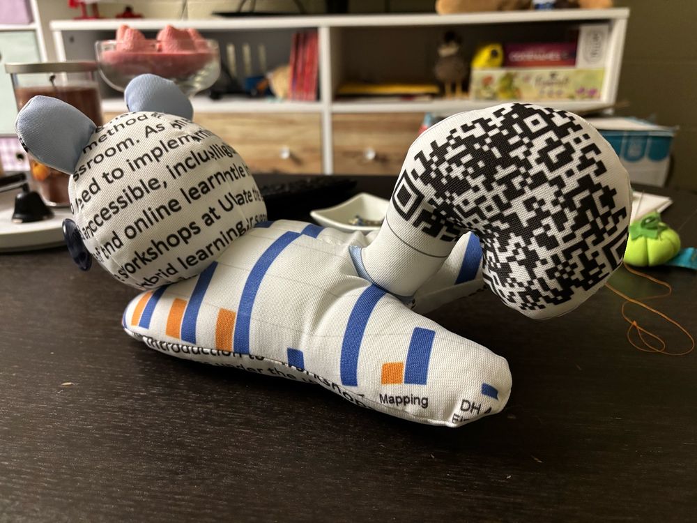 Squirrel plush photographed to better show the body and tail. The body has bar graphs on it, and the tail has QR codes. 