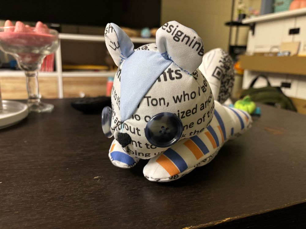Squirrel plush sitting on a table. The head has button eyes and is made of fabric with writing on it. 
