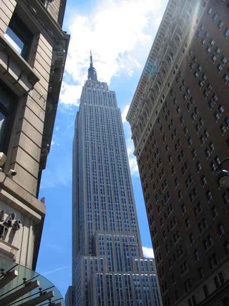 Narrow view of Empire State Building, New York City, framed by buildings on both sides against a background of blue sky and light clouds