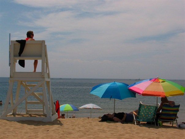 Beach with ocean view, lifeguard on chair on the left, multicolor umbrellas and beach chairs on the right