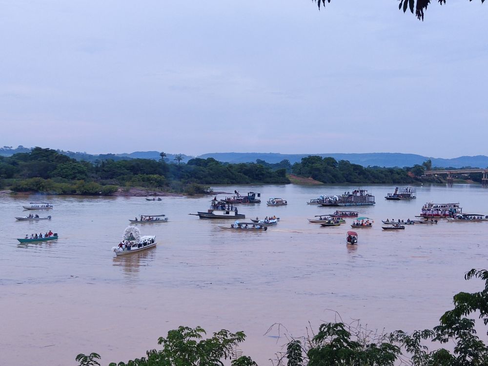 Vários barcos com ornamentação de flores e balões navegando no Rio Fresco. Ao fundo, paisagem de mata e em evidência, o rio com as embarcações.