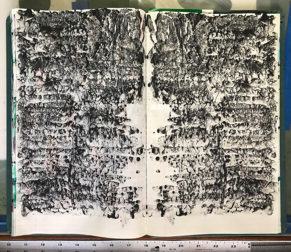 An open sketchbook displaying a symmetrical pattern spread across both pages, the axis of symmetry being the inner margin where the pages are bound together. The pattern stops approximately an inch short of the bottom of the page, where the white paper is left unpainted. The allover pattern is painted in granular black watercolor, uneven and blotchy. One-third of the way down the page, the pattern starts to read as being made up of closely spaced horizontal bands. There are gaps towards the inner margin of the sketchbook, where unpainted white paper forms a symmetrical void.