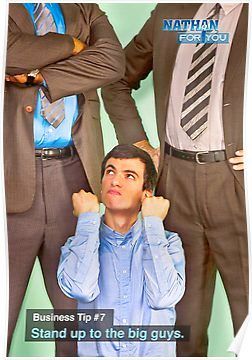 An image of Nathan Fielder kneeling in front of two men in suits with his hands positioned as if he were grabbing their penises.