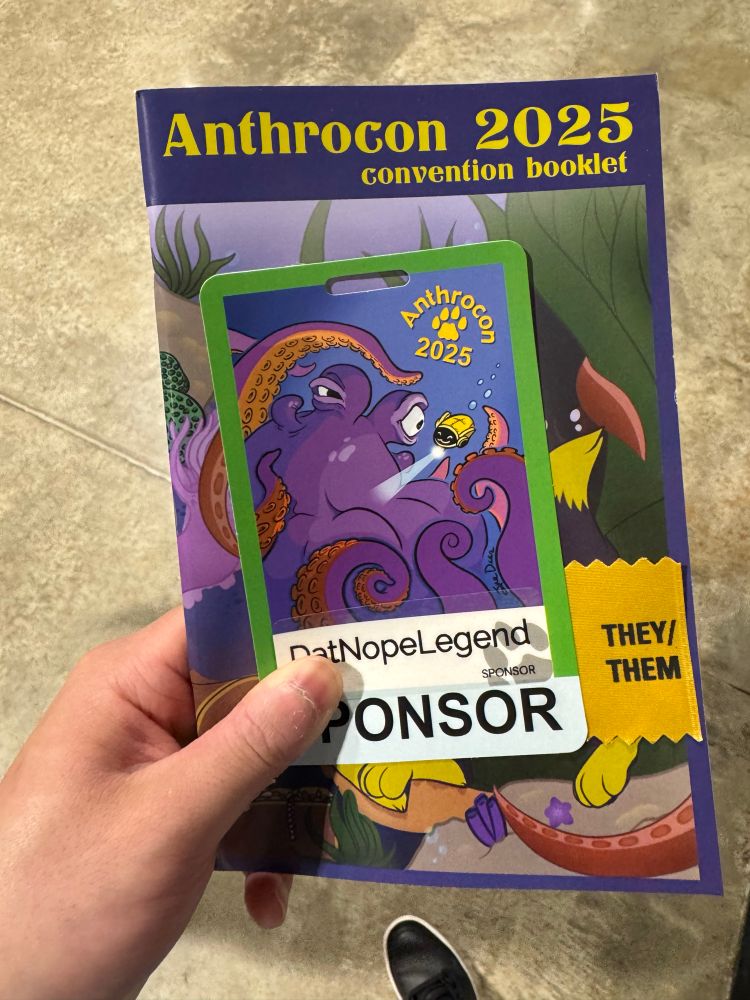 Me holding my 2025 AC con badge and the con book 