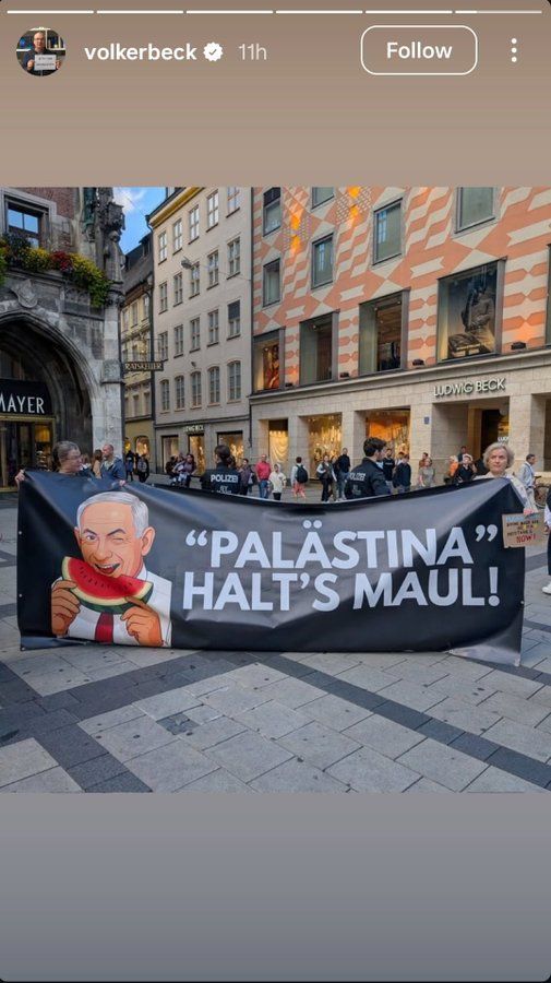 Une banderole portée par deux personnes montre un Netanyahu facétieux faisant un clin d'œil tandis qu'il savoure une tranche de pastèque, à côté du slogan : "Palästina halt's Maul!" (Palestine ferme ta gueule !).