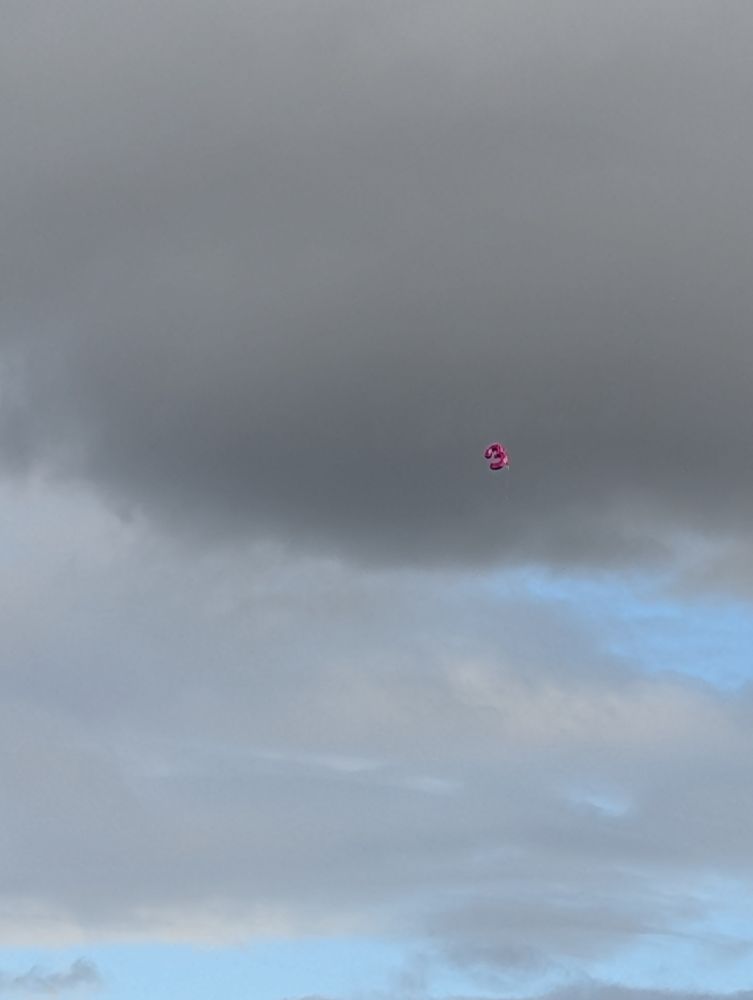 Pink helium balloon in the shape of a 3 floating high in the sky