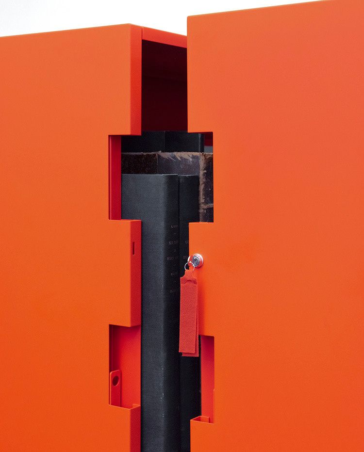 Detail photograph of the opening of a geometric bright orange book case enclosure.