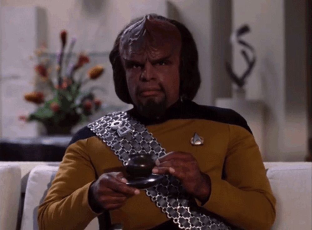 a man in a star trek uniform sits on a couch holding a cup